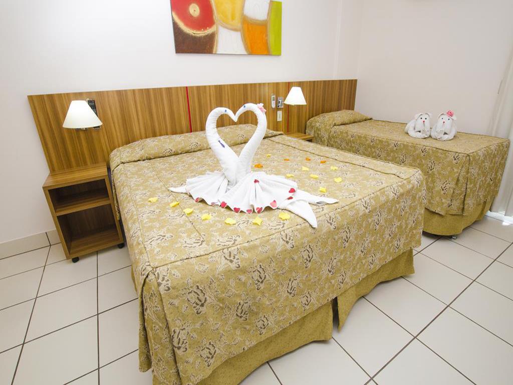 Interior dos quartos do diRoma Exclusive, uma cama de casal e uma de solteiro ao lado, ambas decoradas com toalhas dobradas em forma de Cisnes e filhotes de cachorro.