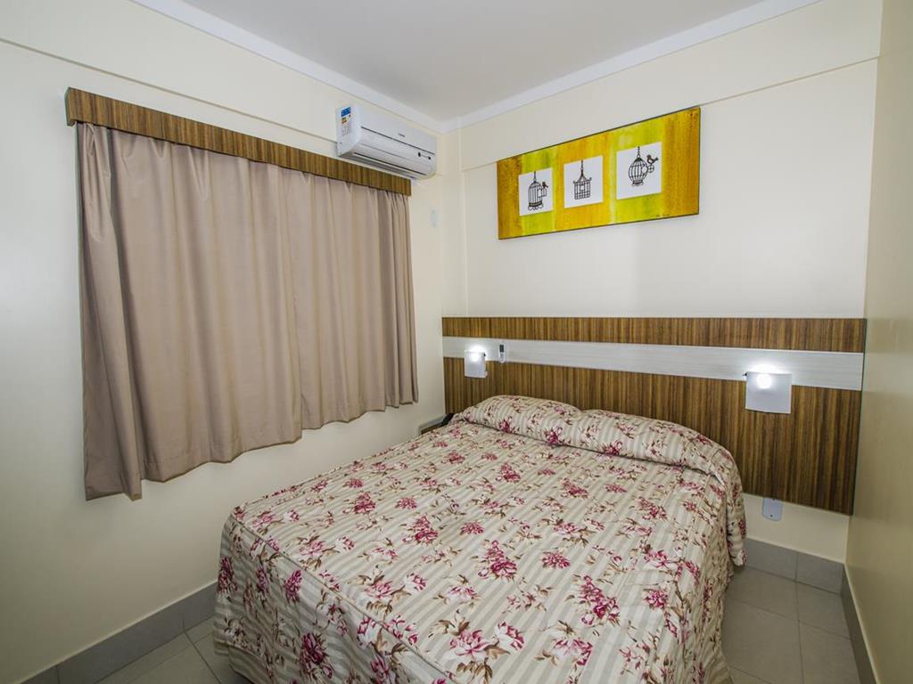 Interior de um quarto no Lacqua diRoma, na imagem vemos uma cama de casal, criado-mudo e ar-condicionado.